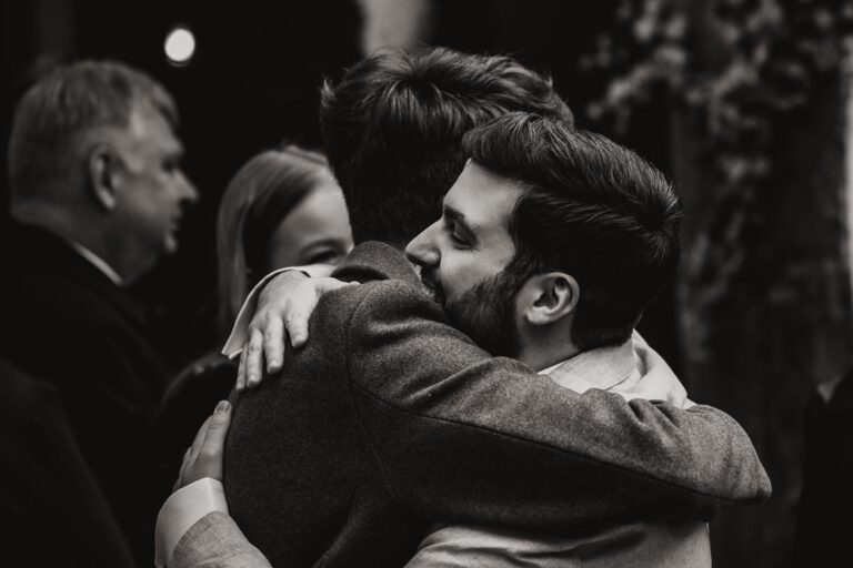 Ein schwarz-weiß Foto auf dem der Bräutigam in Murnau nach der Trauung seinen besten Freund umarmt, die Freude ist den beiden ins Gesicht geschrieben