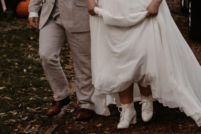 Das Hochzeitspaar läuft in Murnau über den nassen Boden, die Braut hat weiße Stiefel an und hält sich das Kleid hoch, damit es nicht nass wird