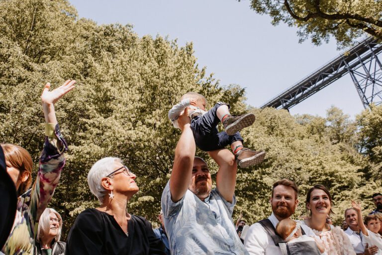 Die Hochzeitsgäste feiern ausgelassen in Solingen, ein Kind wird in die Luft gehoben und jubelt, aufgenommen in Farbe