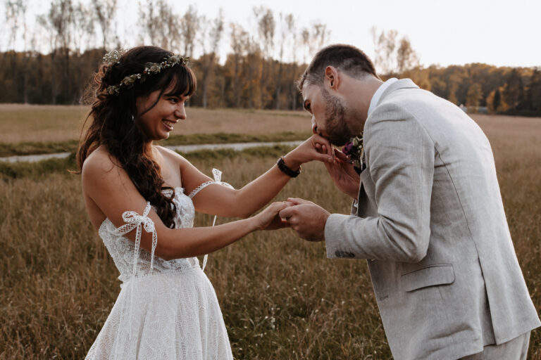 Ein Brautpaar auf einem Feld in Garmisch-Partenkirchen, die Braut hält ihre Hand zum Bräutigam und er gibt ihr einen Handkuss. Aufgenommen in Farbe