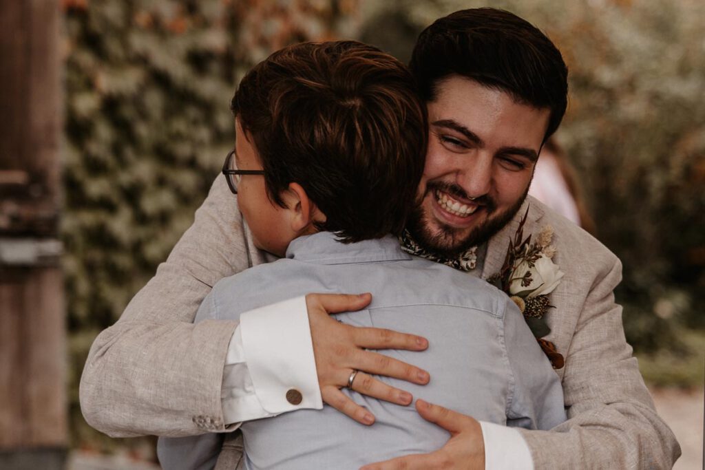 der Bräutigam umarmt ein Kind nach der Hochzeit und lächelt breit in die Kamera, ein emotionaler Moment, aufgenommen in Murnau