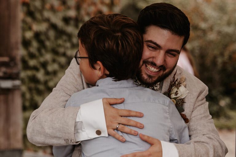 der Bräutigam umarmt ein Kind nach der Hochzeit und lächelt breit in die Kamera, ein emotionaler Moment, aufgenommen in Murnau