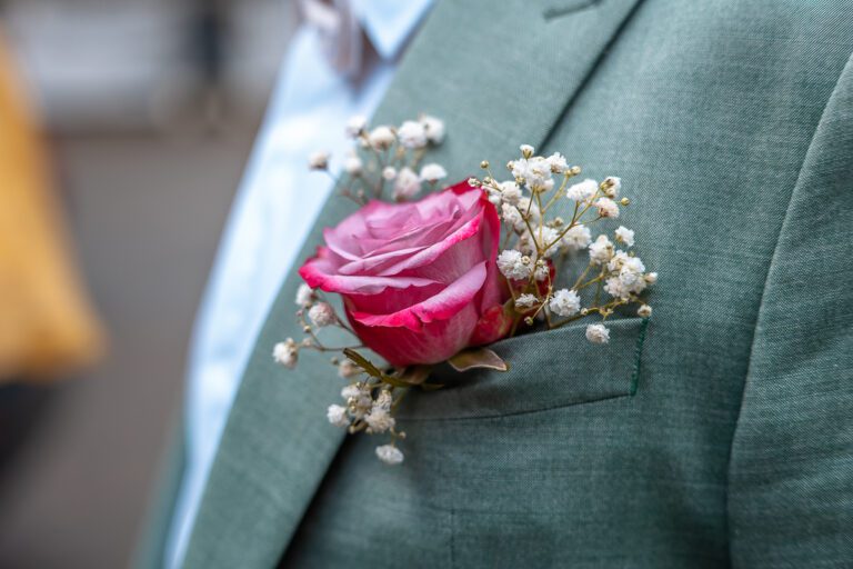 Man sieht auf der Hochzeit in Bayern das Jackett des Bräutigams in türkis mit einer pinken Rose in der Einstecktasche