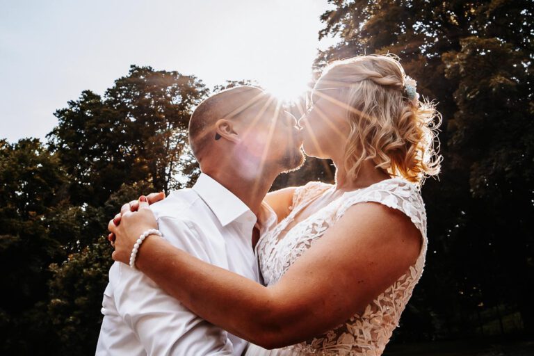 Eure Hochzeitsfotografin in Garmisch-Partenkirchen. Ein Brautpaar küsst sich am Eibsee, die Sonne geht unter und ist genau zwischen den beiden zu sehen, aufgenommen in Farbe. Der perfekte Moment für ein Foto